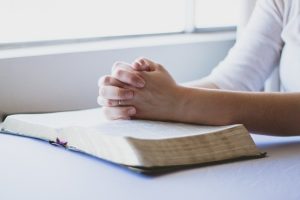 Staying Positive in a Negative World-hand clasped in prayer over a Bible