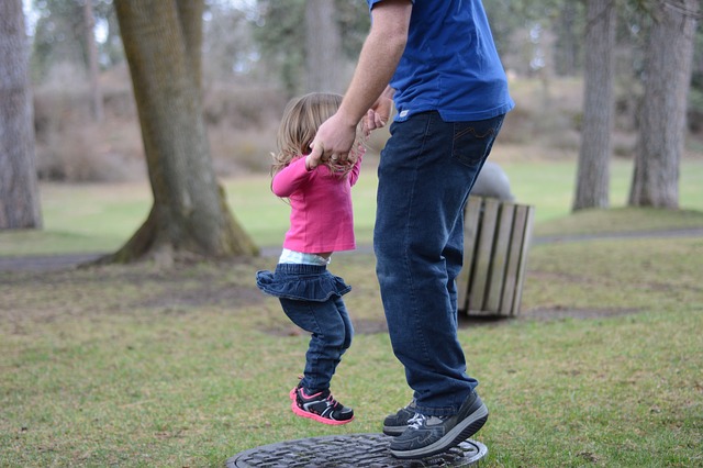 Finding Balance--father holding daughter's hands while she jumps